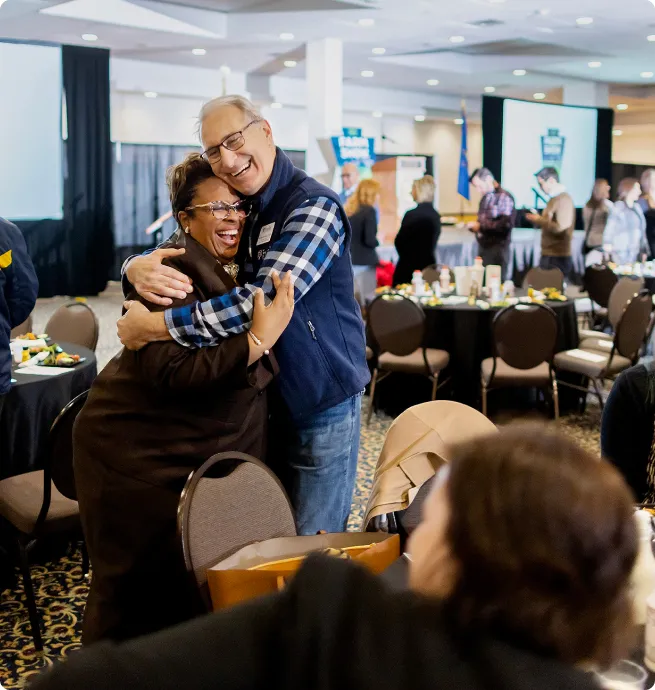 two people smiling and hugging at an event