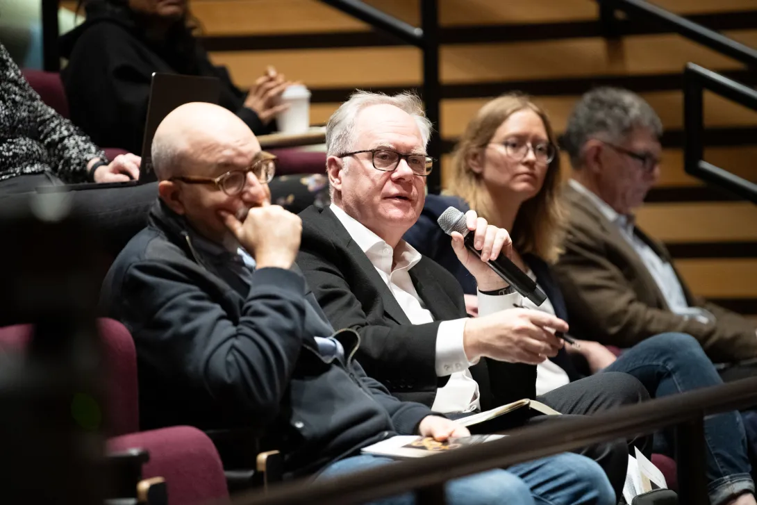 Four people seated in an auditorium, one is holding a microphone