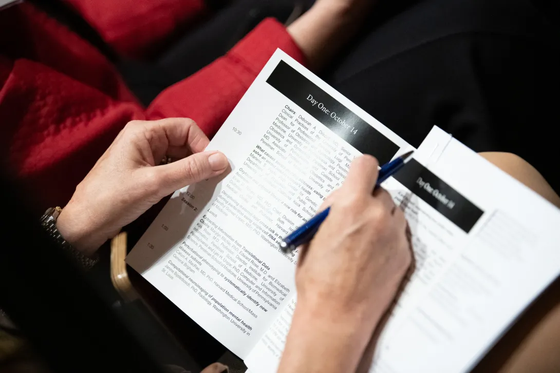 Close up photo of two hands holding a pen and a conference program