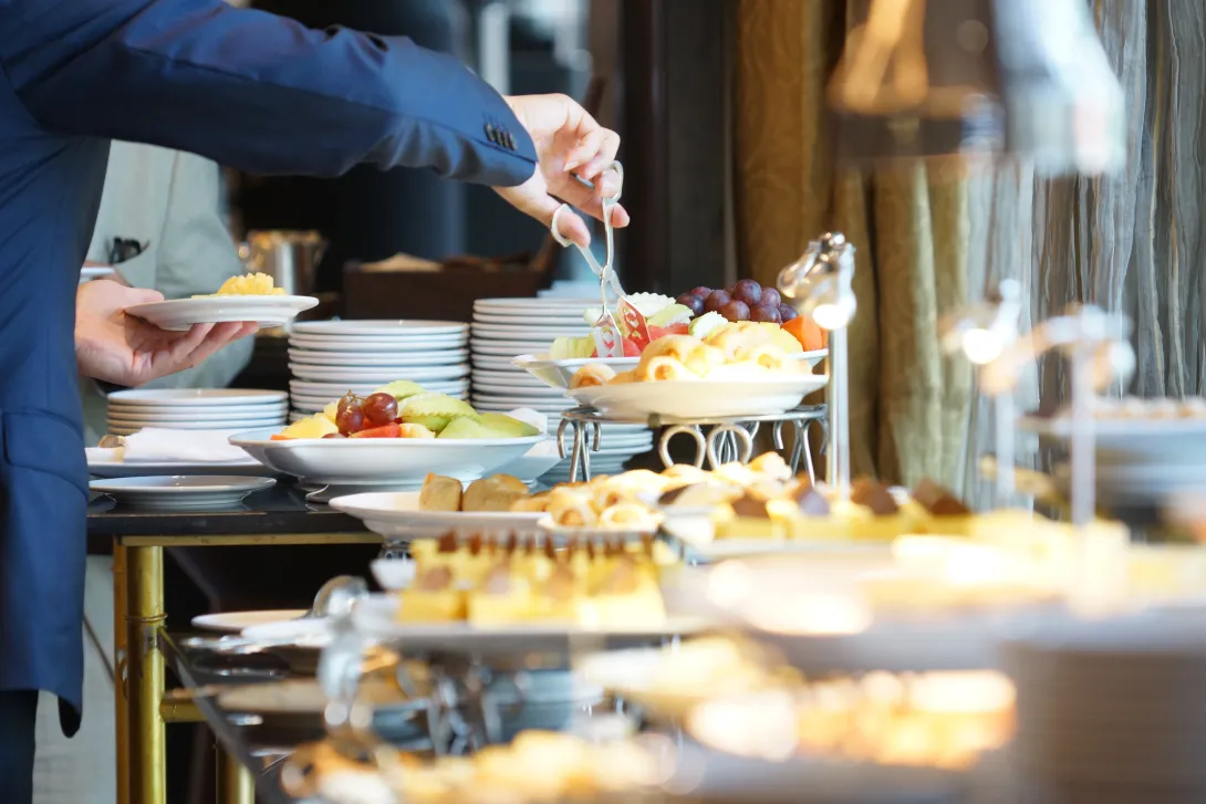 Table set with catering appetizers with a guest using tongs to take an item off of a plate.