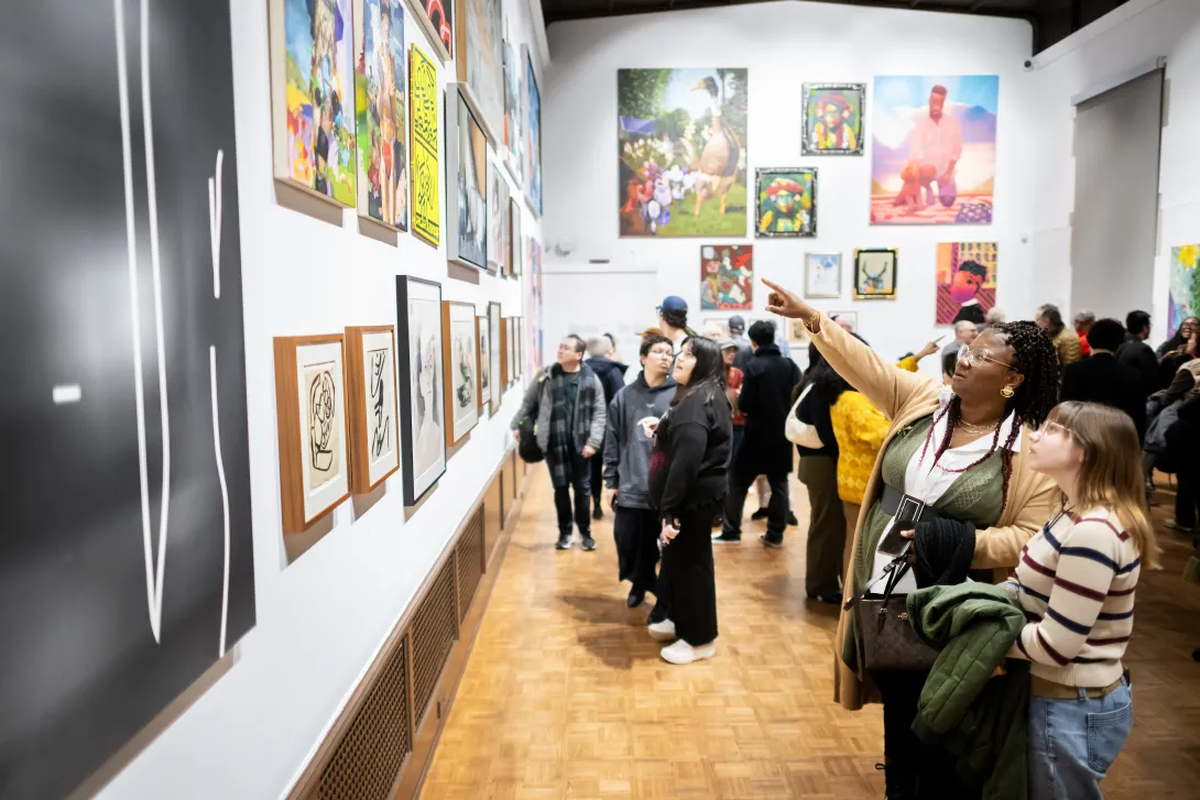 View of an art gallery with two women in front, one is pointing in front of her at art on the wall