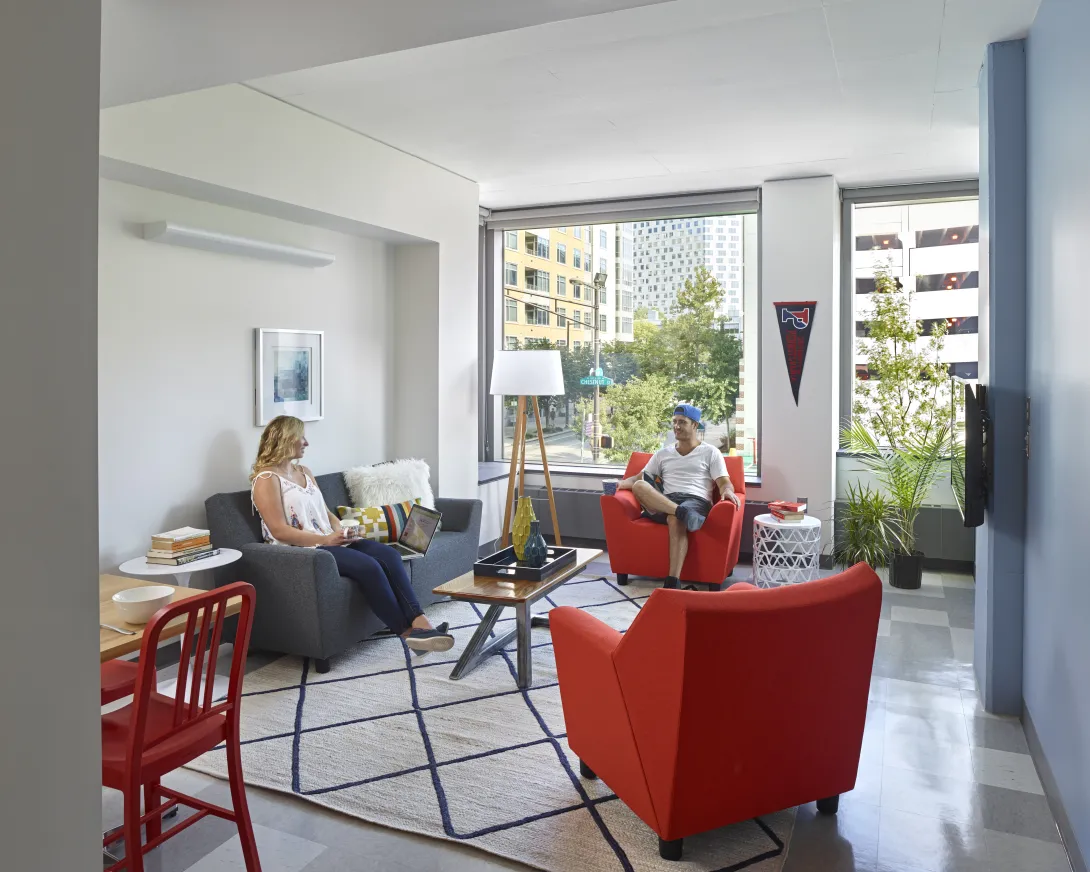 Photograph of a College House living room with two students sitting in chairs having a conversation.