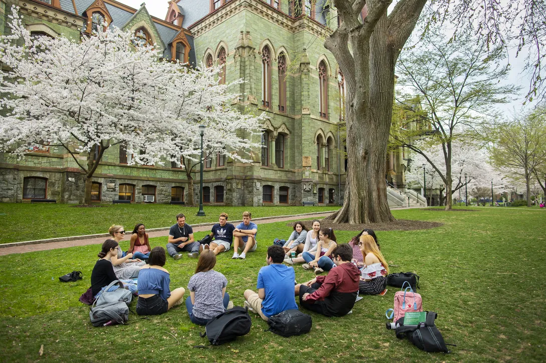 A circle of students sitting on the lawn in front of the University of Pennsylvania's College Hall