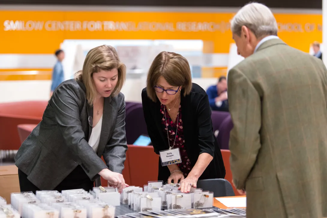 Two women in front of a registration table looking through name badges while a man stands waiting.