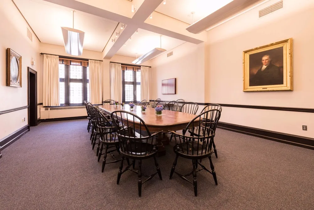 Board room table in center of room with painted portraits hung on in gold frames around the wall