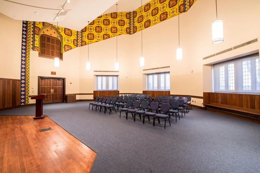 Meeting room with theater style seating arranged in blue chairs in front of a podium. 