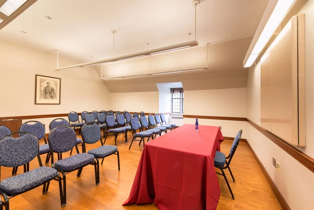 Meeting room with four rows of four chairs set theater style facing a table with a red table cloth