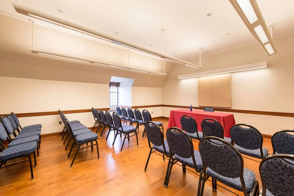 Meeting room with blue chairs in groups of four set theater style facing a table with a red tablecloth