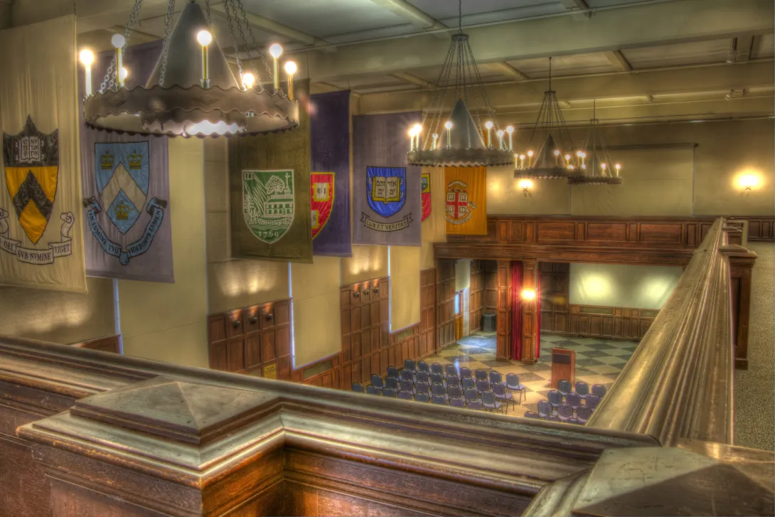 View of Hall of Flags from blacony showing seven Ivy League school flags, as well as blue chairs set theater style facing a podium