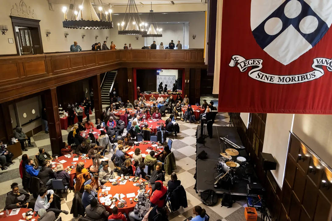 Houston Hall's Hall of Flags full of round tables and people during an event with people looking on from the balcony