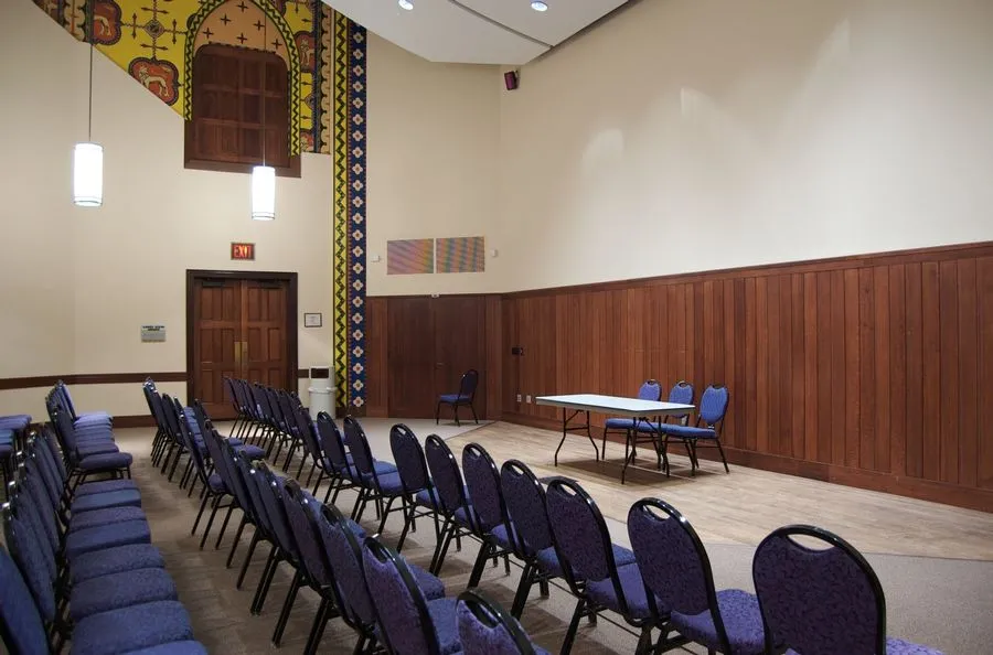 Meeting room set theater style with blue chairs facing a wood paneled wall with a table and three chairs set up